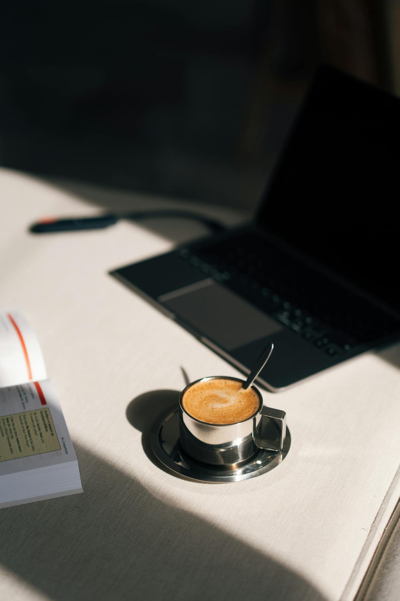A cozy workspace featuring a laptop, an open book, and a freshly brewed coffee.